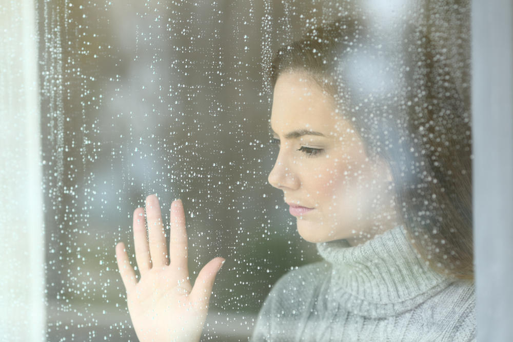 Woman looking through window (The Problems with Cheap Window Replacements)